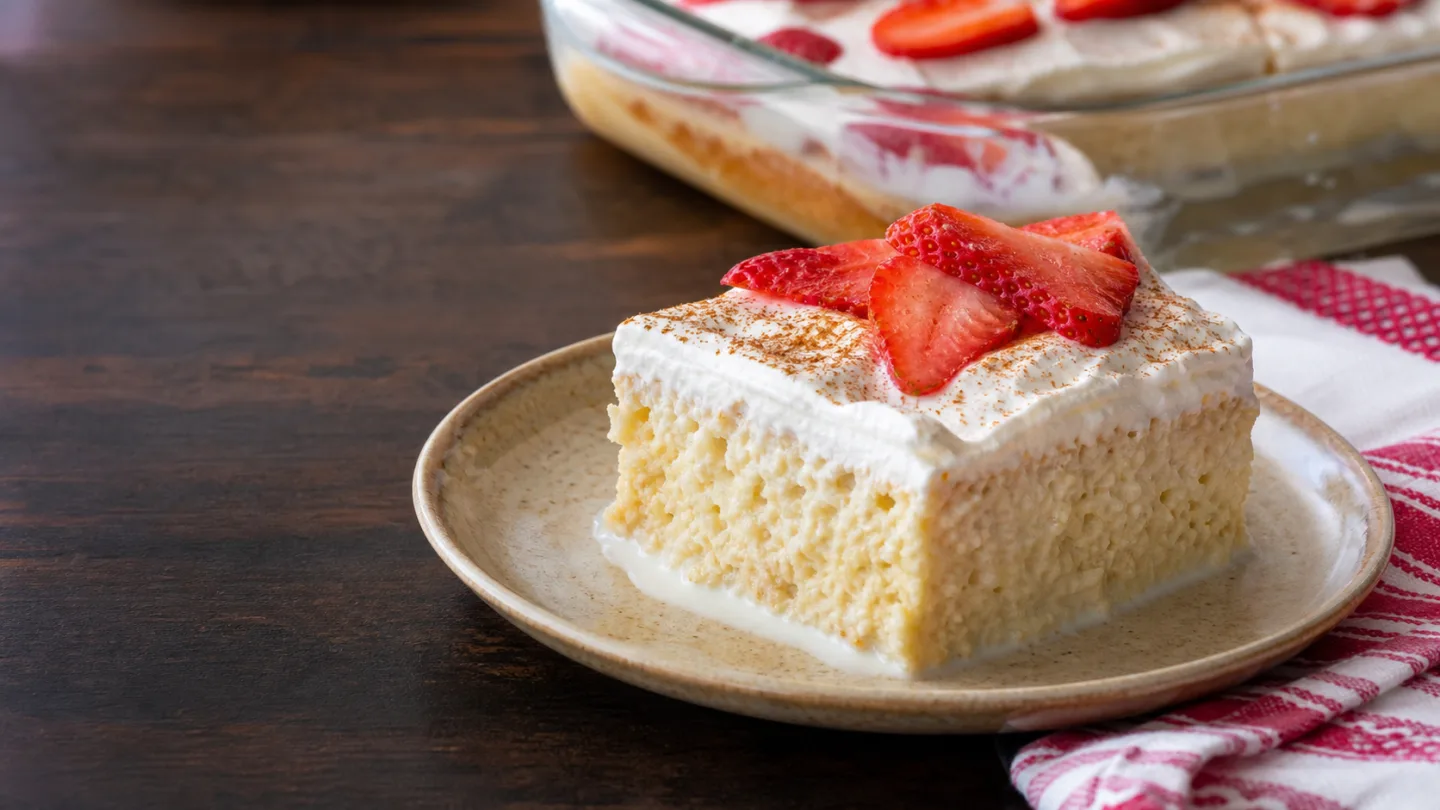 Slice of homemade tres leches cake with whipped cream, strawberries, and cinnamon